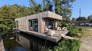 Een drijvend woonboot met een dek, zithoek en een klein zwembad.