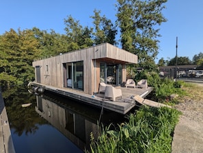 Een drijvend woonboot met een dek, zithoek en een klein zwembad.