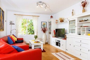 Ein Wohnzimmer mit einem roten Sofa, einem Fernseher, weißen Schränken und einem Fenster mit Vorhängen.