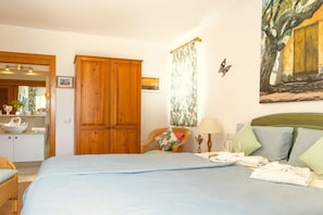 Ein Schlafzimmer mit einem Bett, einem Holzschrank, einem Stuhl, einem Tisch mit Lampe und einem Bild an der Wand.