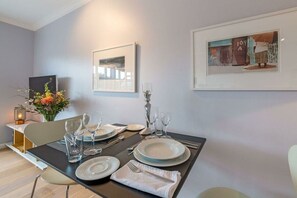 A dining area with a table set for four, a vase with flowers, and framed artwork on the wall. - Holiday apartment with 1 bedroom (Kampen)