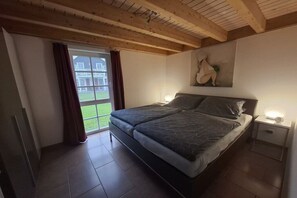 Et soveværelse med en seng, to sengeborde, en lampe på væggen, et vindue med gardiner og udsigt til en bygning.