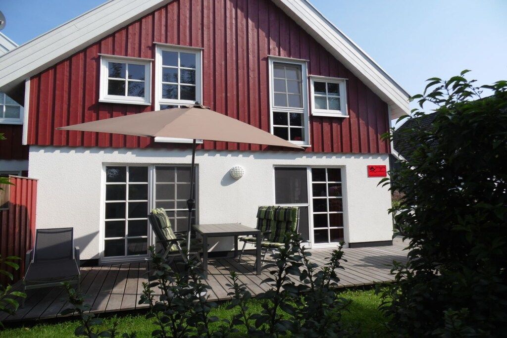 A two-story house with a red exterior, white trim, and a covered patio area with outdoor furniture.