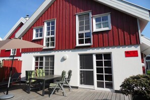 A red and white building with a patio area featuring a table and chairs. - Holiday home with 3 bedrooms (Krummhörn*\/Greetsiel)