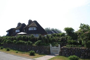 Ein großes Haus mit einer Steinmauer und einem weißen Tor, umgeben von üppiger Bepflanzung.