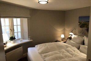 Ein Hotelzimmer mit Bett, Nachttischlampen, einem Fenster mit Vorhängen, einem Heizkörper und einem Wandbild.