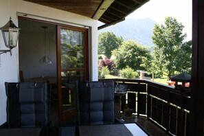 A balcony with a view of trees and mountains, a chair, a table, and a lamp. - Holiday apartment with 3 bedrooms (Rettenberg)