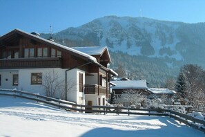 A wooden chalet with a balcony, surrounded by snow-covered ground and mountains. - Holiday apartment with 3 bedrooms (Rettenberg)