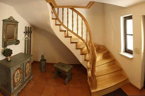 A staircase with wooden handrails and steps, a small stool, a cabinet with decorative items, and a mirror on the wall. - Holiday home with 2 bedrooms (Schönbrunn)