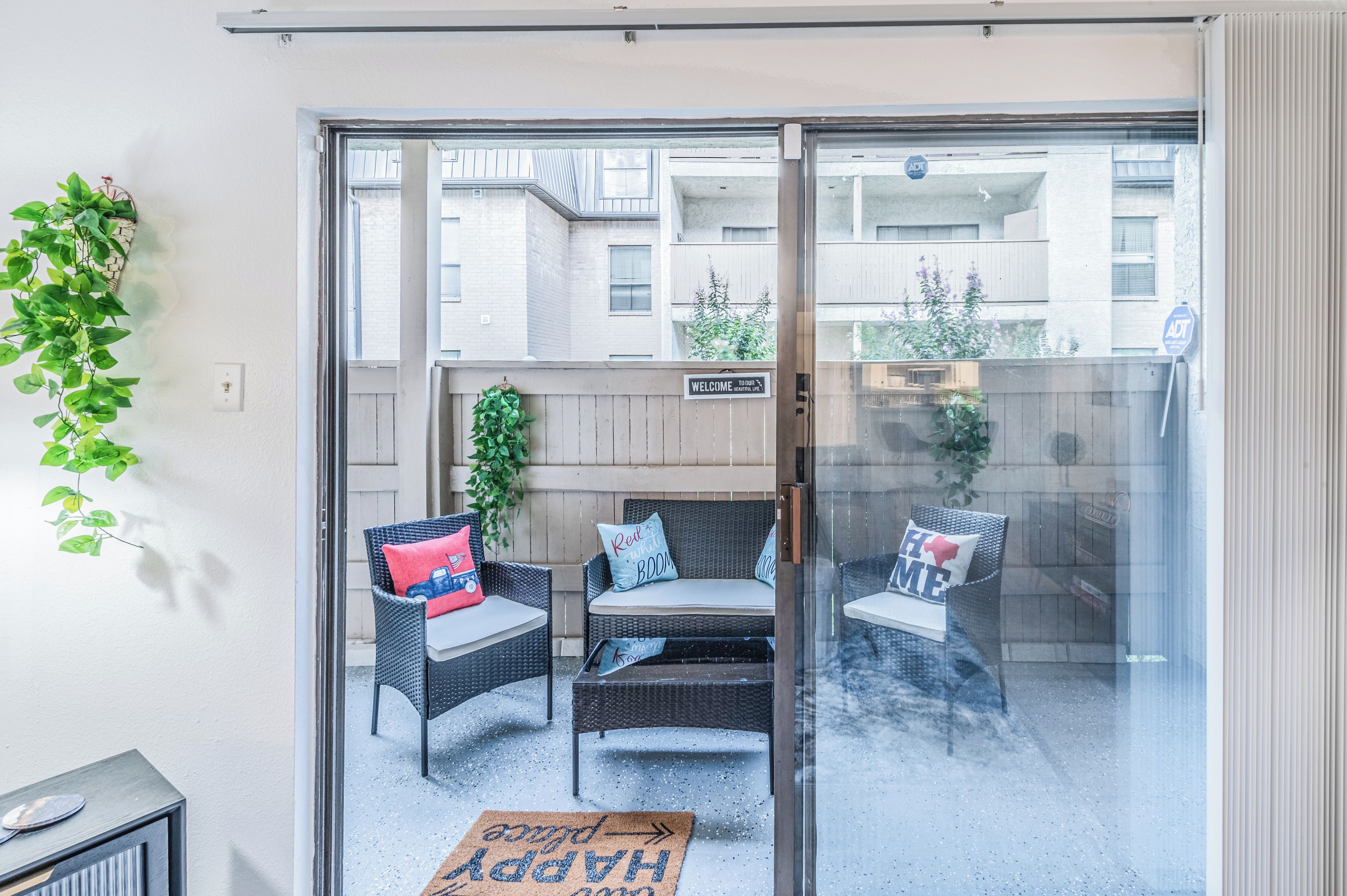 A glass door leading to an outdoor seating area with wicker furniture and cushions.