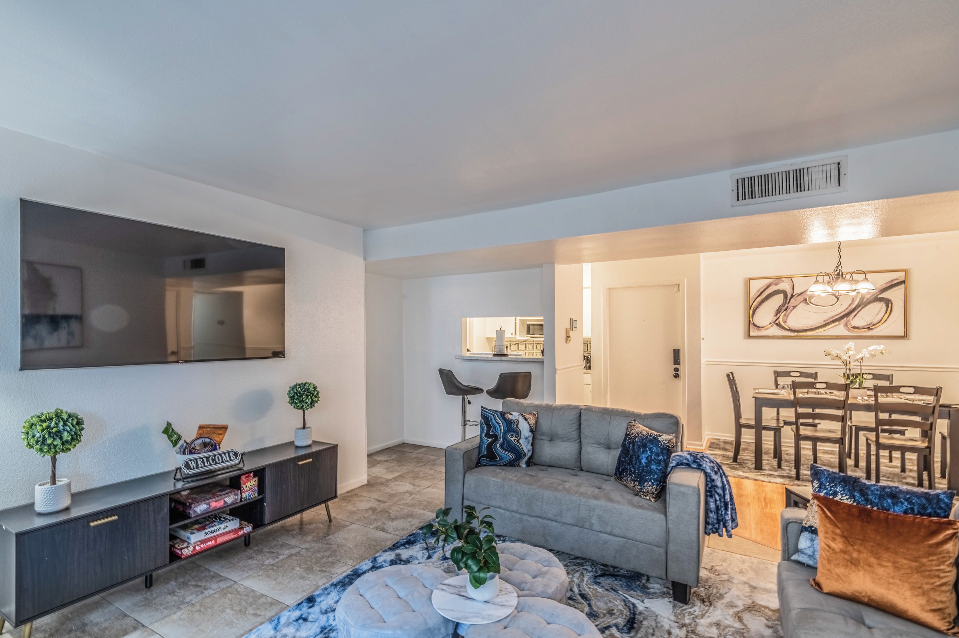 A modern living room with a grey sofa, a coffee table, and a dining area with a chandelier.