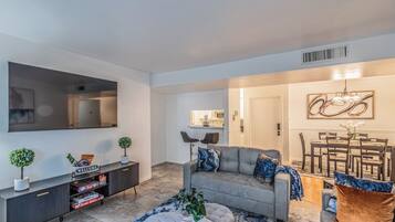 A modern living room with a grey sofa, a coffee table, and a dining area with a chandelier.