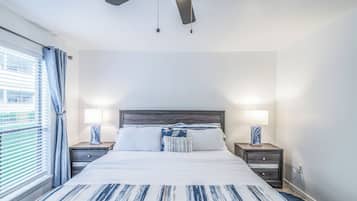 A bedroom with a bed, two bedside tables, a ceiling fan, and a window with curtains.