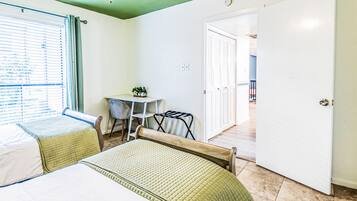 Ein Hotelzimmer mit zwei Betten, einem kleinen Tisch mit Pflanzen, einem Stuhl und einer Tür zu einem weiteren Raum.