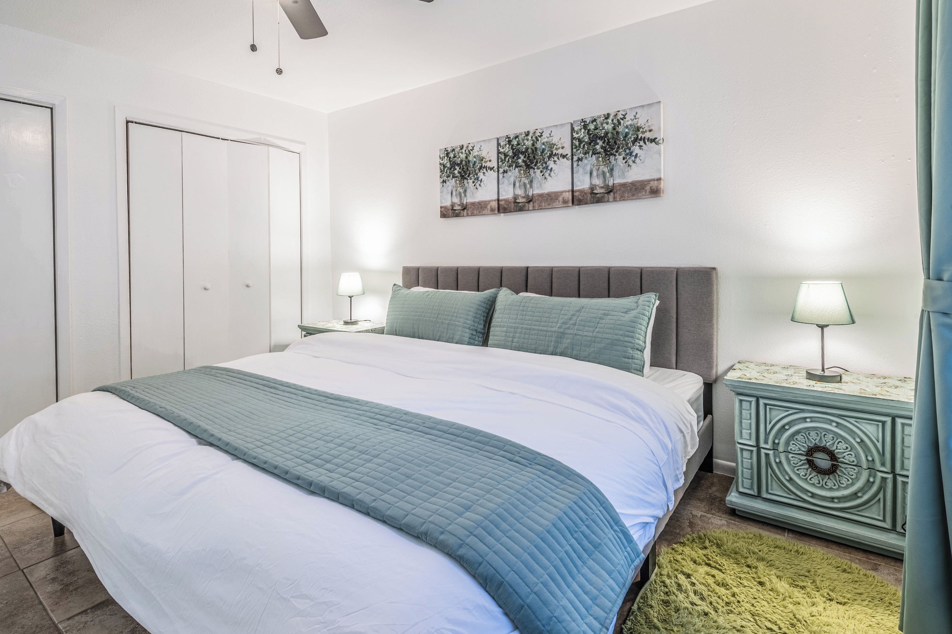 A bedroom with a bed, bedside tables, a headboard, a wall-mounted artwork, and a door.