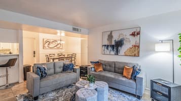 A modern living room with a grey sofa set, a coffee table, and a dining area in the background.
