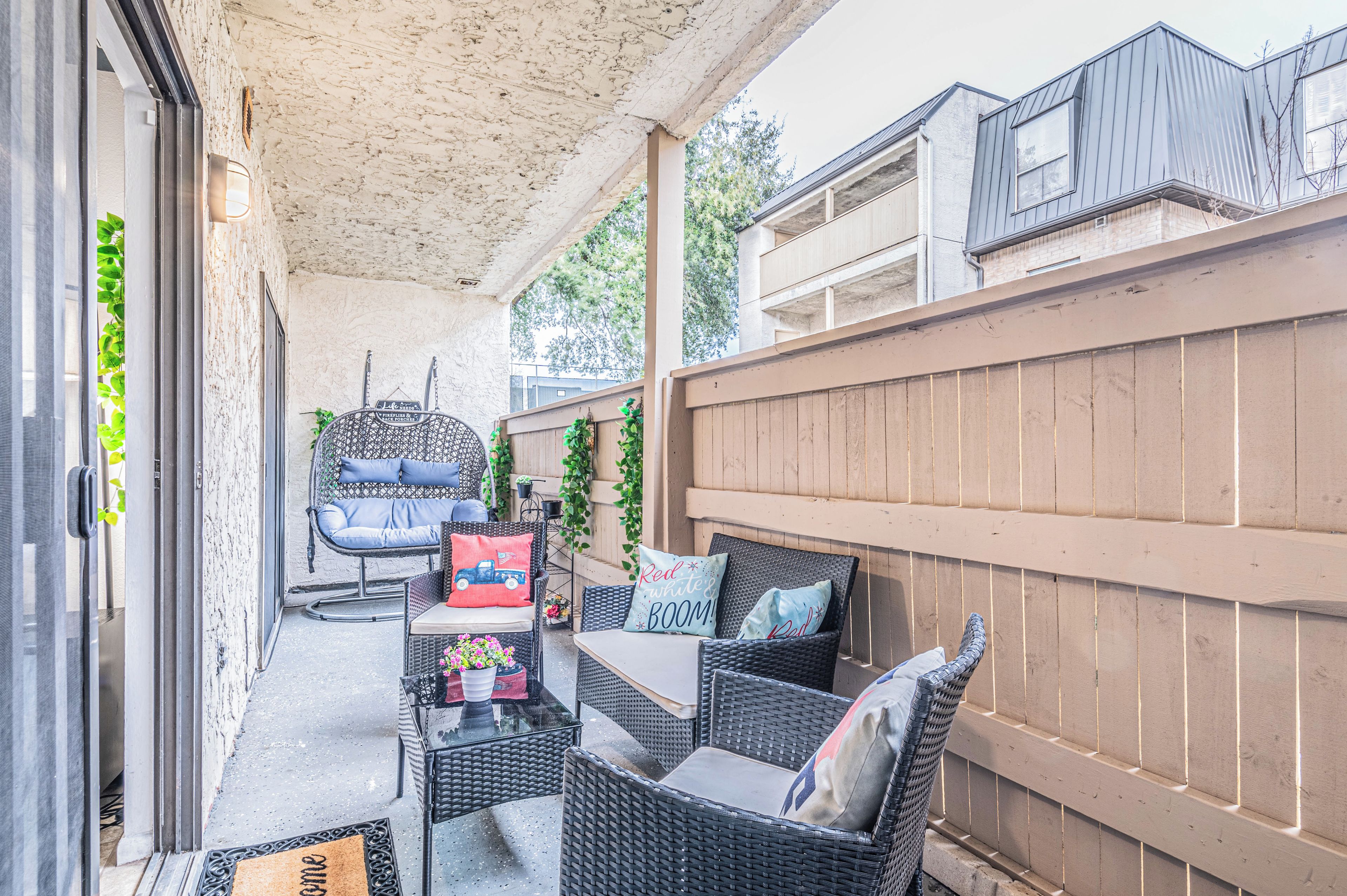 A covered patio area with wicker furniture, a table, and a chair.