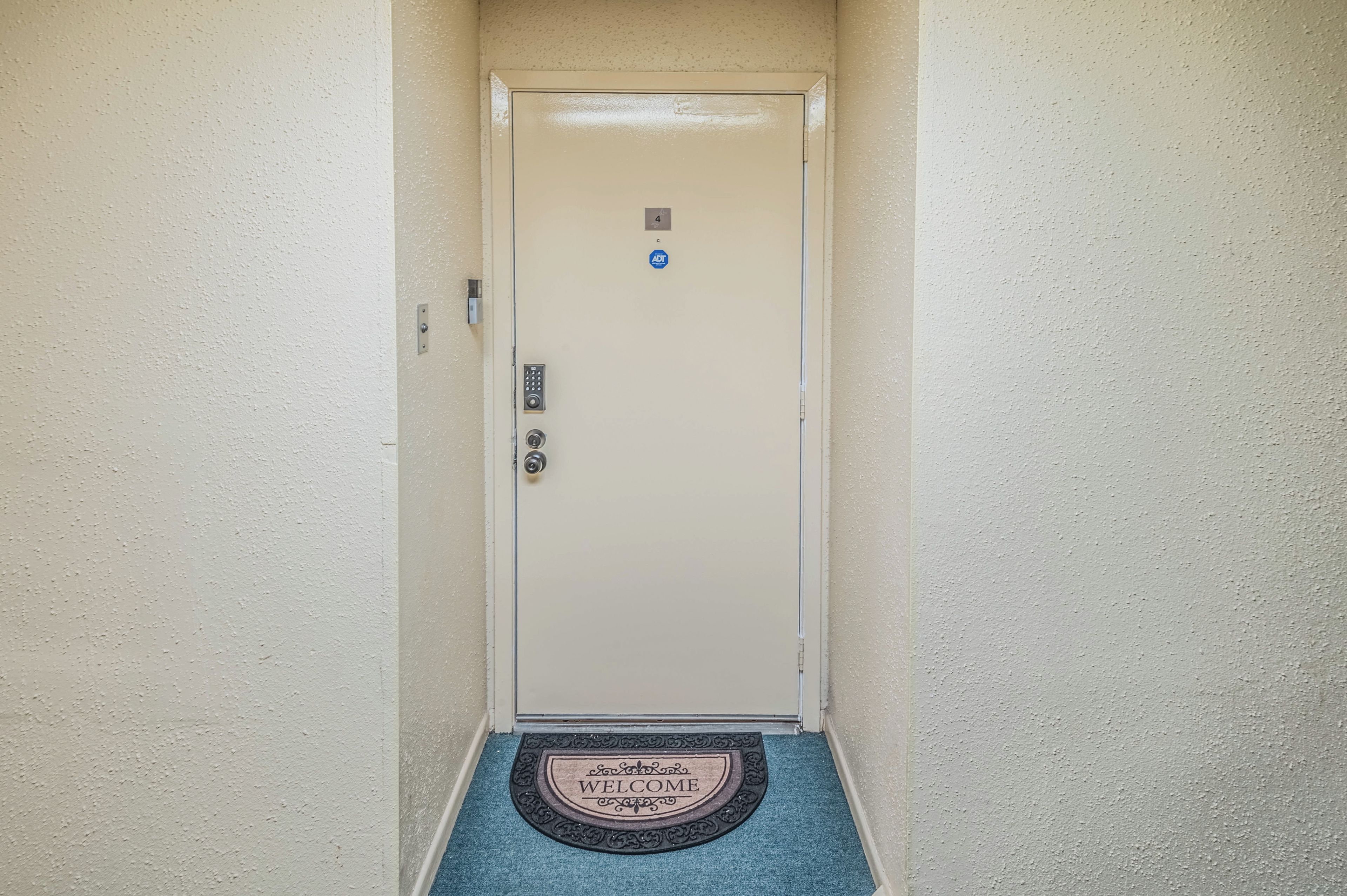 A door with a keypad lock, a doorbell, and a 'WELCOME' mat at the entrance.