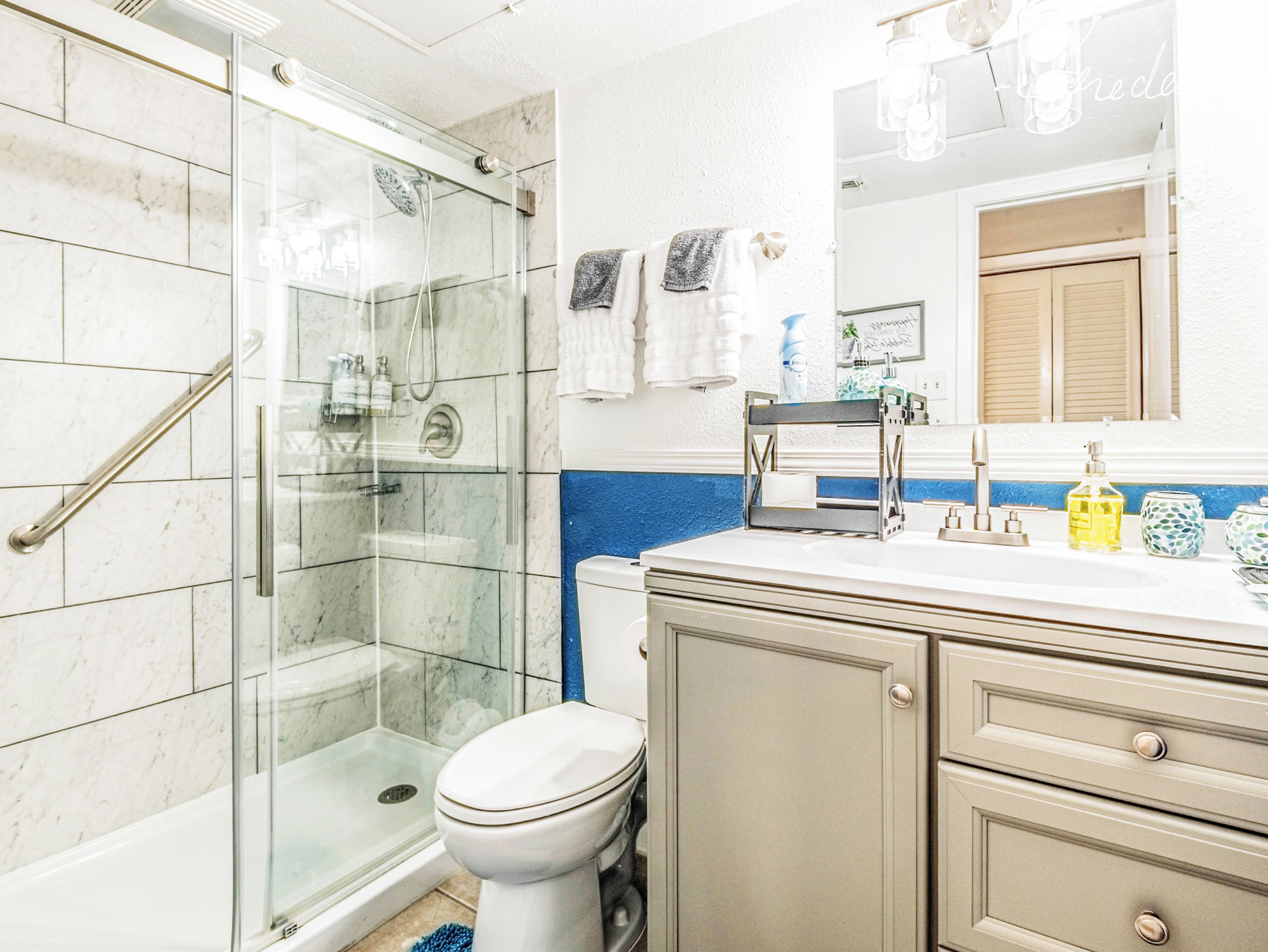 Une salle de bain avec une douche à parois de verre, des toilettes, un lavabo avec un miroir au-dessus et un meuble avec des tiroirs.