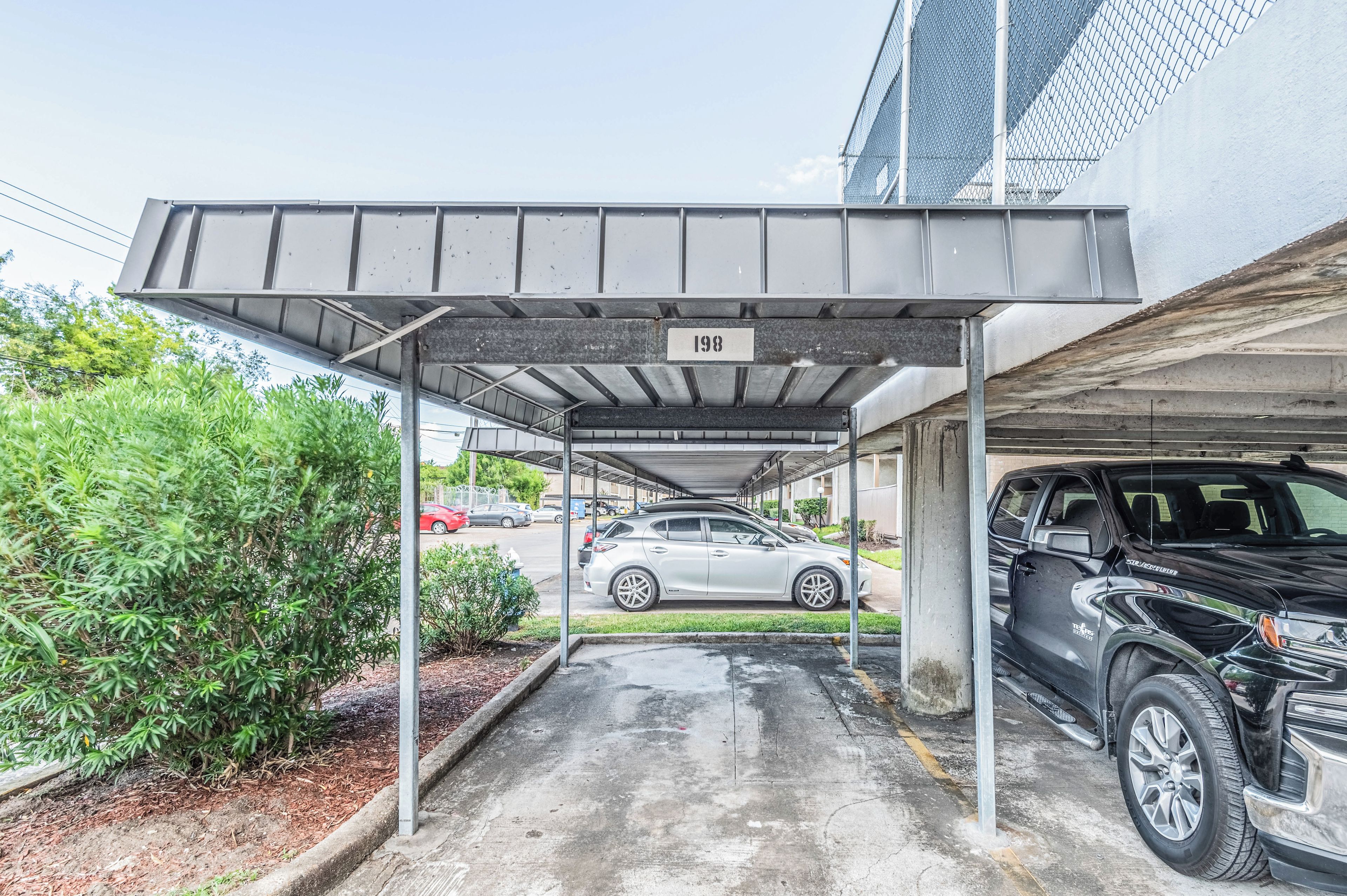 A covered parking area with a numbered sign, a white car, and a black SUV parked.