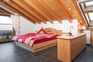 A bedroom with a wooden bed, a small bedside table, and a view through a window. - Holiday apartment with 2 bedrooms (Oberstdorf)