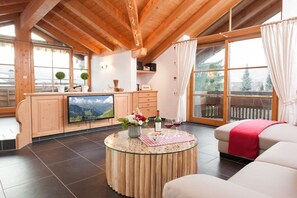A cozy living room with a wooden ceiling, a flat-screen TV, a round glass coffee table, and a sofa with a red throw. - Holiday apartment with 2 bedrooms (Oberstdorf)