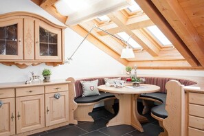 A cozy attic room with a wooden bench, a round table, and a cabinet with glass doors. - Holiday apartment with 2 bedrooms (Oberstdorf)