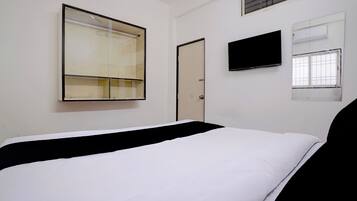 A hotel room with a bed, a television, a window, and a door.