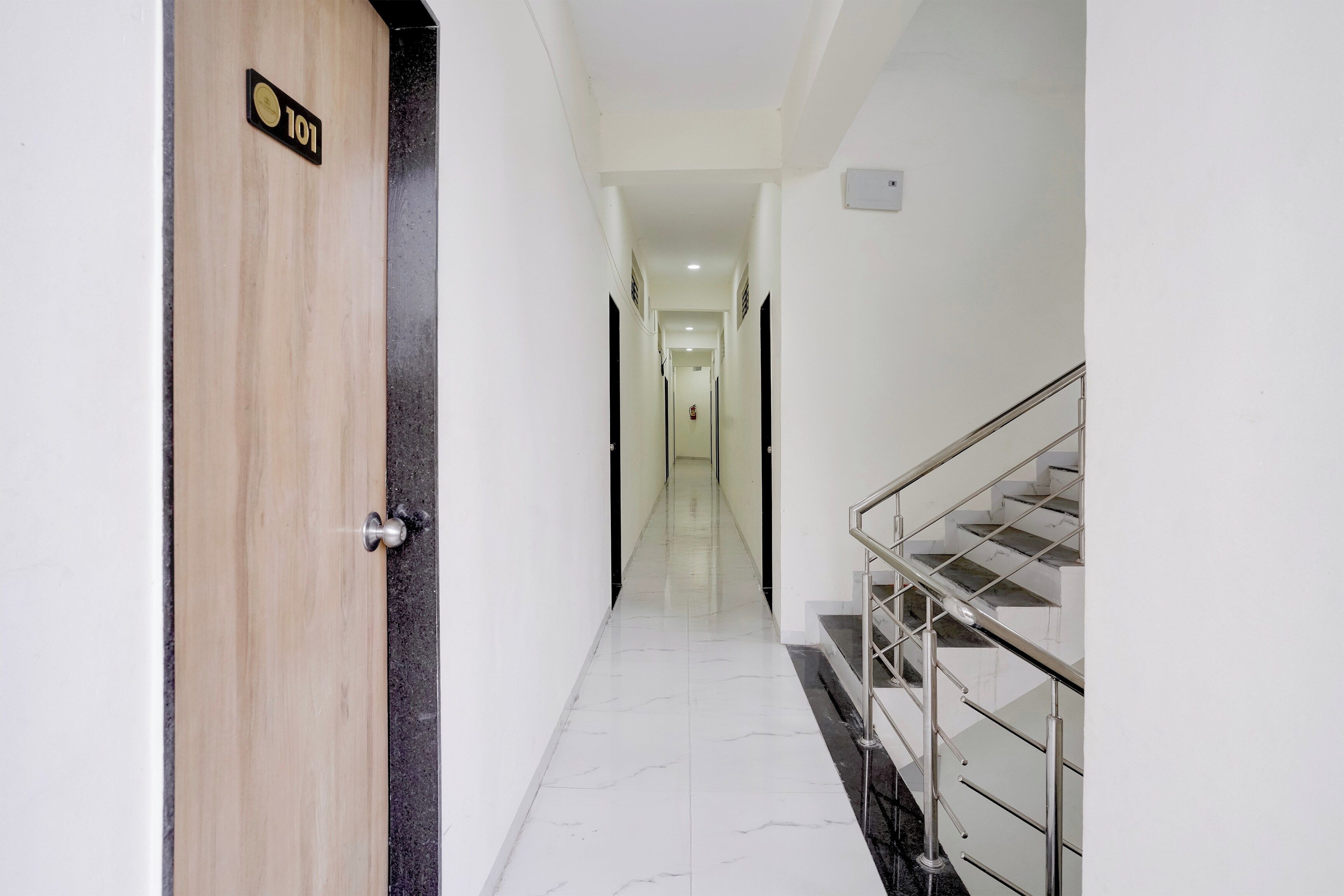 A hotel corridor with a wooden door marked '101', a marble floor, and a staircase with metal railings.