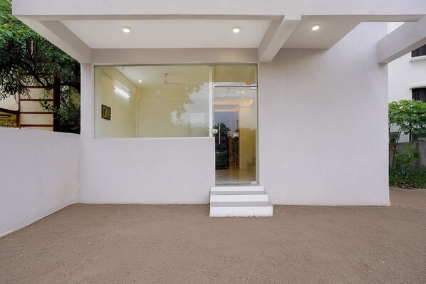 A modern building with a glass entrance, white walls, and a concrete ground.