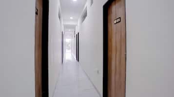 A corridor with wooden doors, white walls, and a marble floor.