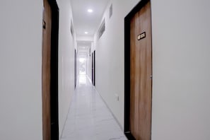 A corridor with wooden doors, white walls, and a marble floor.