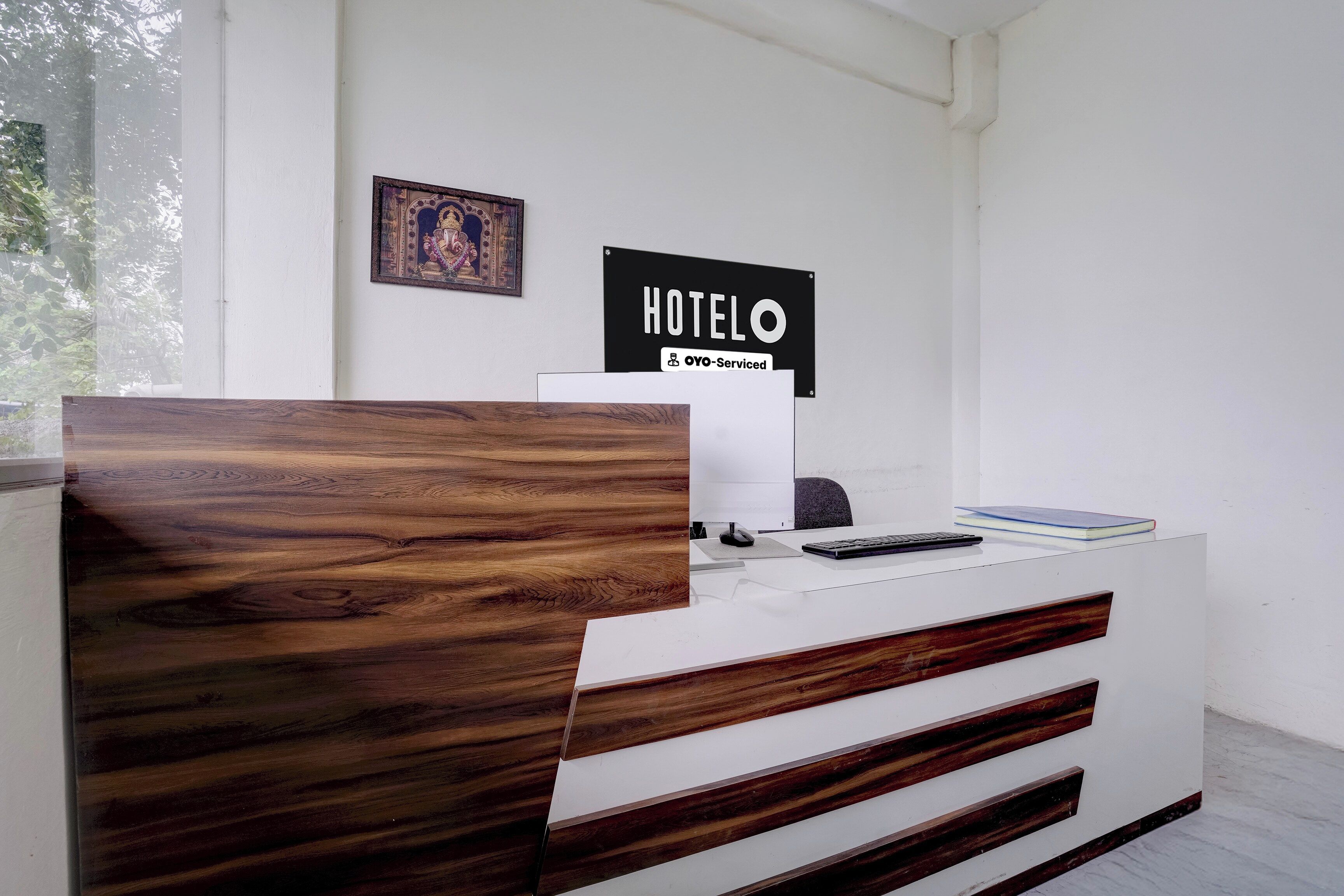 A reception desk with a wooden headboard, a sign reading 'HOTEL OYO-Serviced', and a framed picture on the wall.