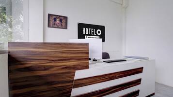 A reception desk with a wooden headboard, a sign reading 'HOTEL OYO-Serviced', and a framed picture on the wall.