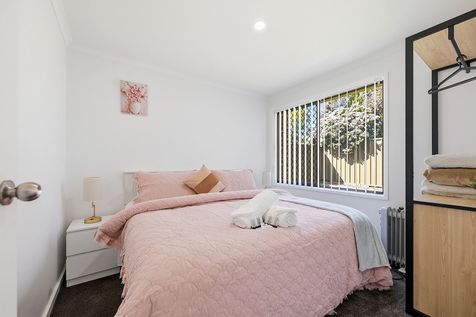 Une chambre à coucher comprenant un lit, une table de chevet, une lampe, une fenêtre donnant sur des arbres et un radiateur.