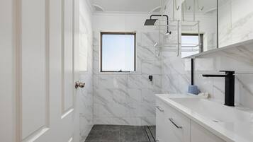 Un baño moderno con pared de mármol blanco, una ventana, una ducha y un lavabo con grifo negro.