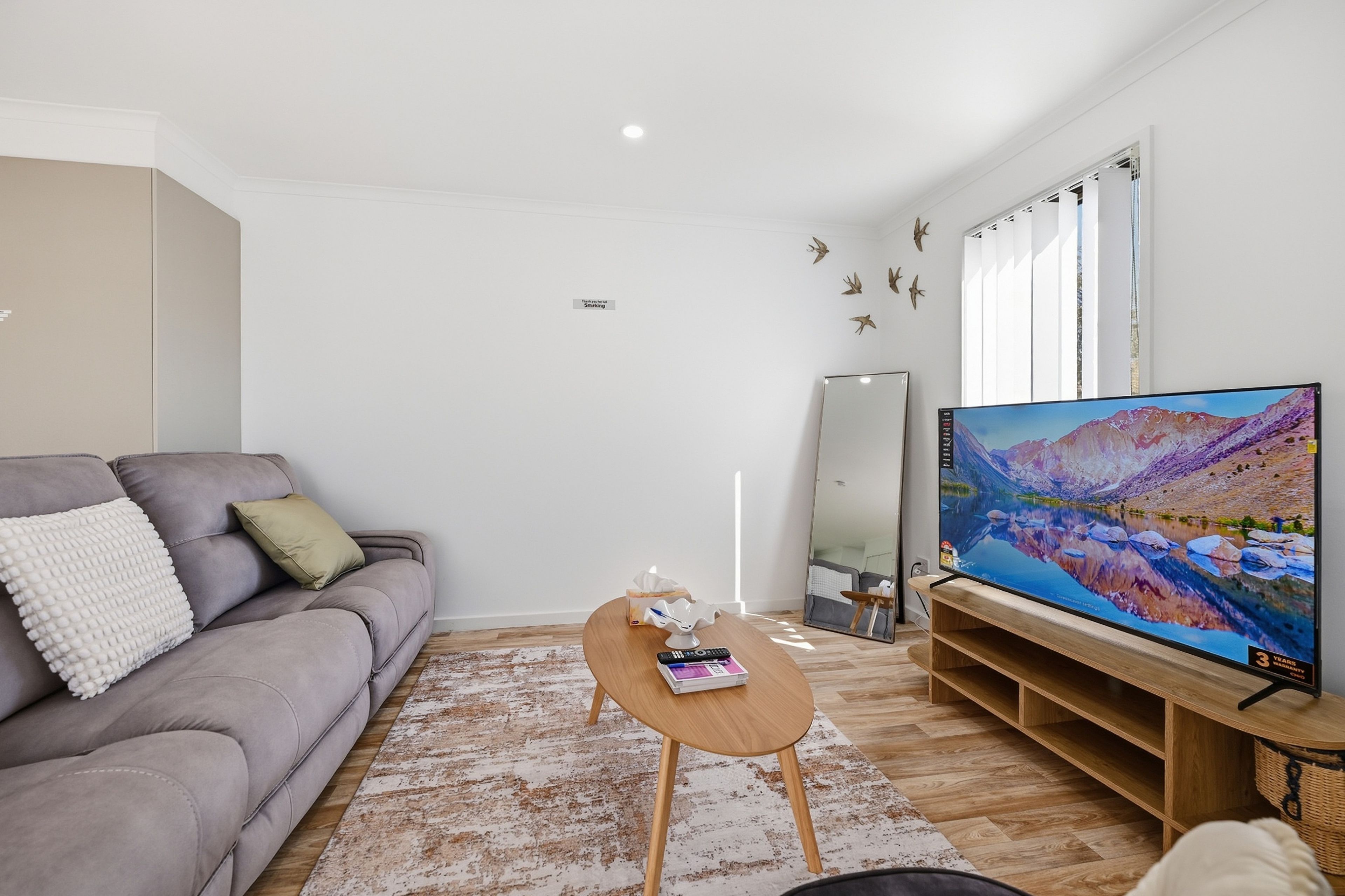 Een woonkamer met een grijze bank, een salontafel, een flatscreen televisie en een grote spiegel.
