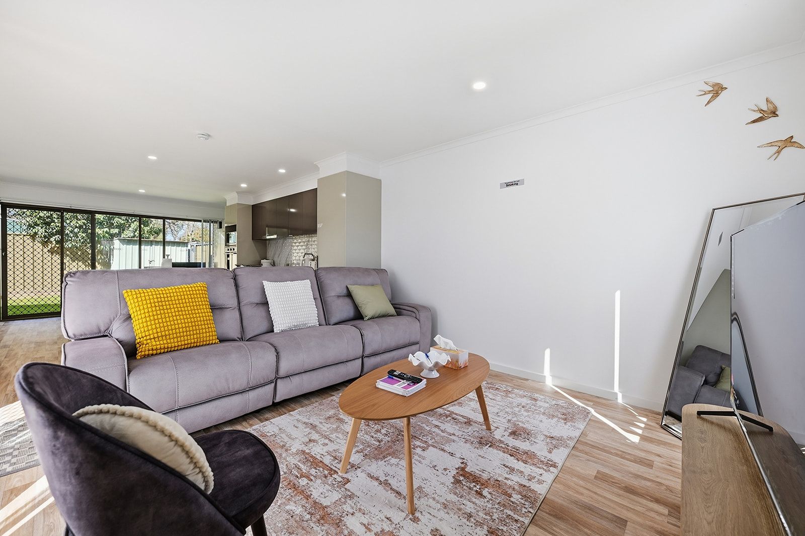 A modern living room with a grey sofa, a wooden coffee table, and a black armchair.