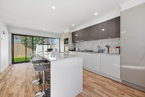 A modern kitchen with a central island, bar stools, and a sliding glass door leading to a backyard. - Chic & Fresh: Newly renovated home retreat (Orange)
