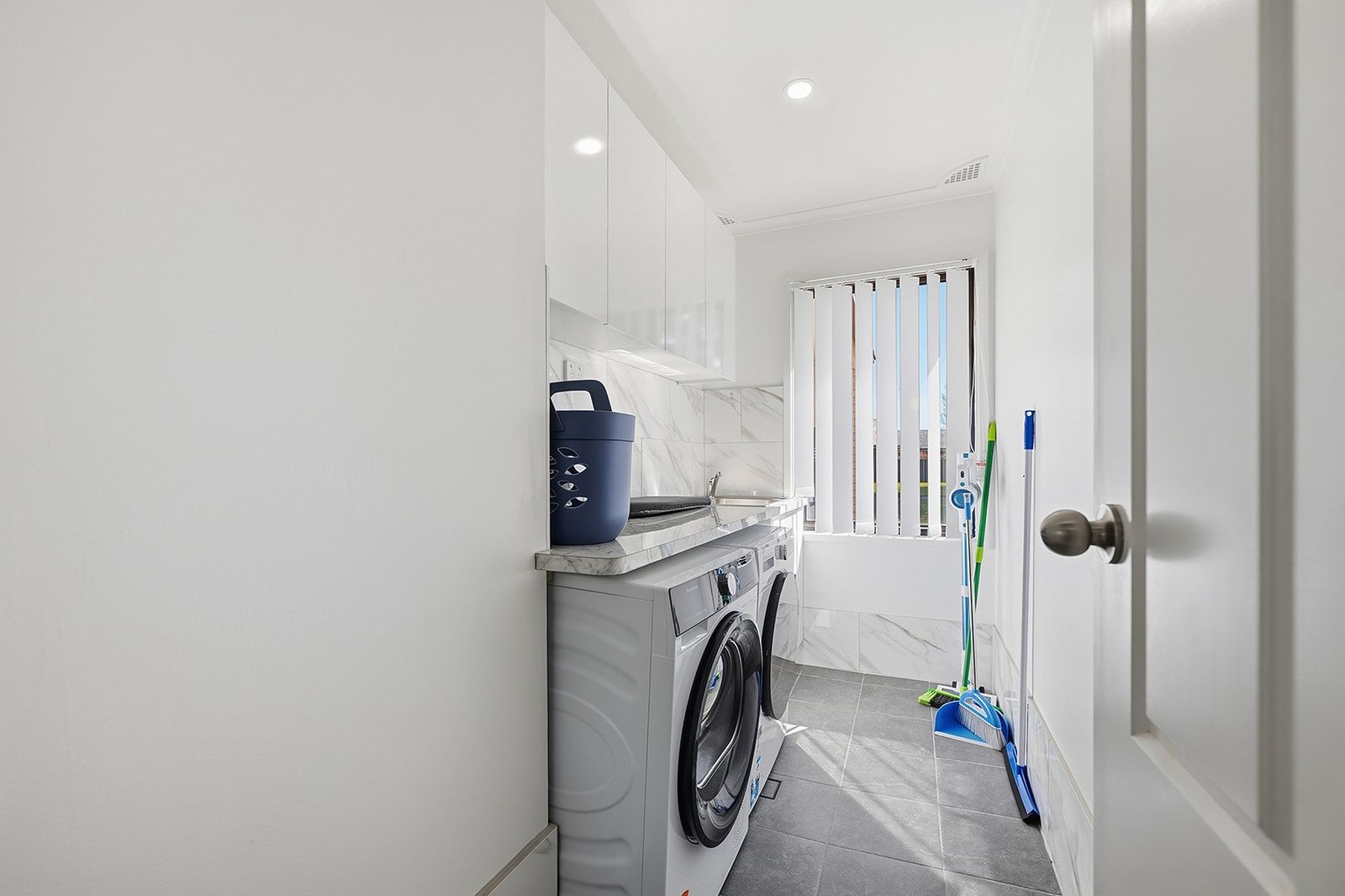 A laundry room with a washing machine, a drying rack, and a blue bucket.