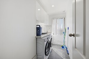 A laundry room with a washing machine, a drying rack, and a blue bucket. - Chic & Fresh: Newly renovated home retreat (Orange)