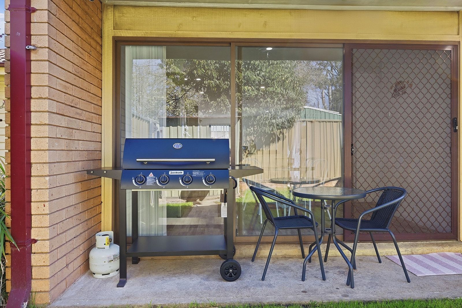 En grill med betjeningsknapper, gasbeholder og et bord med stole i en baghave.