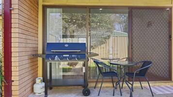 En grill med betjeningsknapper, gasbeholder og et bord med stole i en baghave.