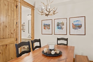 A dining area with a wooden table, chairs, a chandelier, and three framed landscape paintings on the wall. - Evenlight Retreat: Sunset Views, Hot Tub, Game Room, A/C | Eagle's Nest (Elk Park)