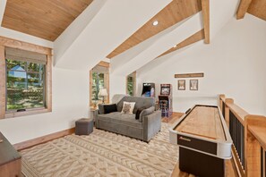 A spacious living room with a pool table, a sofa, and a window overlooking a forested area. - Evenlight Retreat: Sunset Views, Hot Tub, Game Room, A/C | Eagle's Nest (Elk Park)