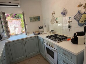 Una cocina con estufa a gas, horno y ventana con puerta abierta.