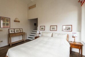 A bedroom with a large bed, a wooden nightstand, a bedside table, a lamp, and a staircase leading to an upper floor. - Trastevere Luxury Panoramic Terrace (Roma)