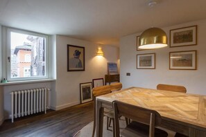 A dining area with a wooden table and chairs, a radiator, a window with a view, and framed pictures on the wall. - Trastevere Luxury Panoramic Terrace (Roma)