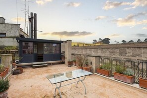 A rooftop patio with a glass table, potted plants, and a view of the cityscape. - Trastevere Luxury Panoramic Terrace (Roma)