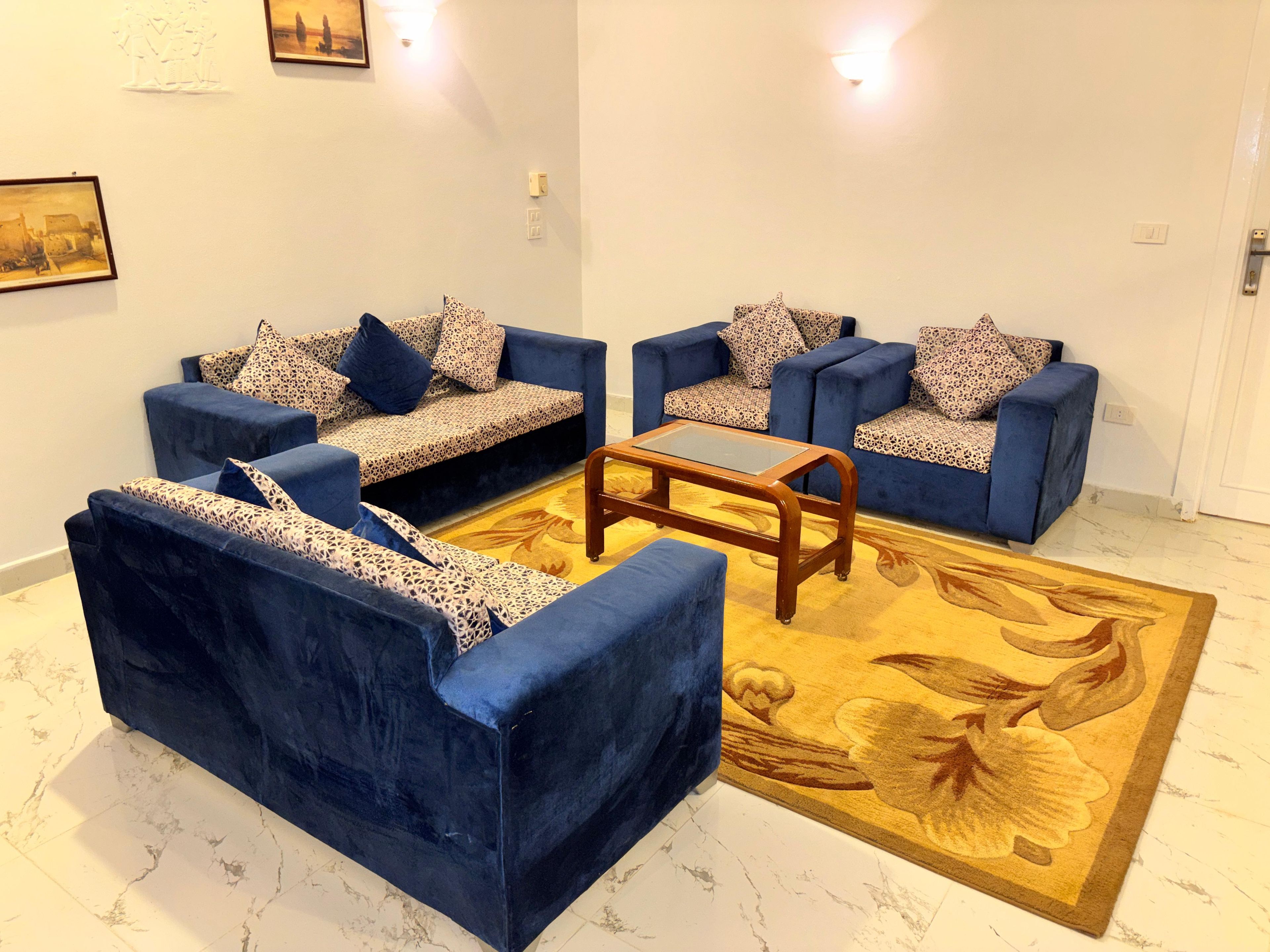 A living room with two blue sofas, a glass coffee table, and a patterned rug.
